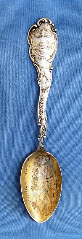 Souvenir Mining Spoon Bonanza Mine.JPG - SOUVENIR MINING SPOON BONANZA MINE ROBINSONVILLE OR - Sterling silver spoon with engraved mine scene in gold washed bowl, marked BONANZA MINE BAKER CITY, ca. 1895, marked Sterling with an S maker’s mark on reverse, made by the Shepard Mfg. Co. Melrose Highlands, MA 1893-1923, handle is marked OREGON with 1859 and crest at top, length 5 1/2 in. and weight 20.3 g,  [The Bonanza Gold Mine was the largest and probably the most valuable free gold mine in the Pacific Northwest in the 1890s.  It was located at the head waters of Burnt River at an elevation of 5,140 feet, about four miles southeast of Robinsonville in Baker County, Oregon, or approximately 40 miles west of Baker City. Discovered in 1877 by a pioneer prospector named Jack Haggard, it was worked by the original locators for two years, reducing the quartz and gold vein ores by the arrastra process. In 1879 the Bonanza Mining Co. purchased it, and erected a ten stamp mill. They continued operations, but failed to make a success of it, and finally closed down.  In 1892 the Geiser Company headed by Al Geiser purchased it, reopened the old works and had the mine and mill in continuous operation until it was sold in 1898, producing nearly $3 million in gold over that period as the heaviest producer in the state. The mine continued in operation till 1907 but little is known after that.  Most recently, a Canadian firm named the Marathon Gold Corp. of Toronto bought the Bonanza in 2012 from the Gazelle Land and Timber LLC of Canyon City with plans to conduct exploratory work.]